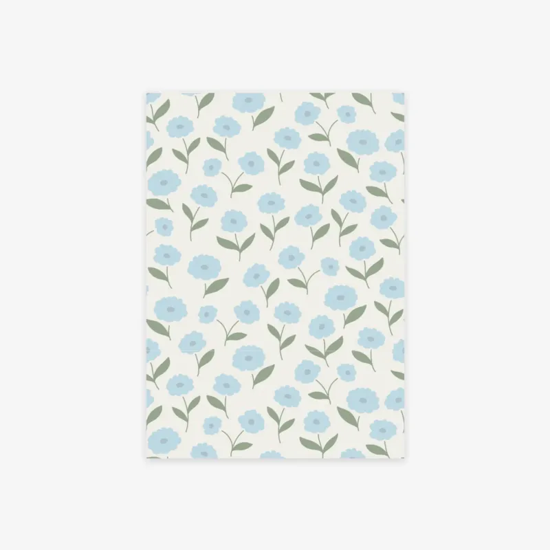 A rectangular sheet of paper with a repeating floral pattern of light blue flowers and green leaves on an off-white background, shown against a light gray studio backdrop.