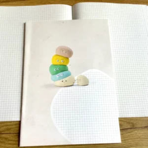 Ein kariertes Heft, das nicht nach Schule aussieht: süße bunte Knetfigur (Fantasiefigur) mit lustigem Gesicht auf dem Cover. Weiß, kariert mit schmalem Rand, durch eine Linie abgetrennt.